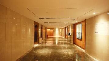 A hotel corridor with a polished marble floor, a wooden door at the end, and a sign indicating room number F12.