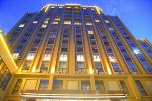 Un edificio alto y moderno con fachada simétrica, amplias ventanas y una entrada destacada en la base.