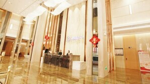 Uma área de recepção de hotel com piso de mármore, um balcão de recepção e um grande elemento decorativo vermelho.