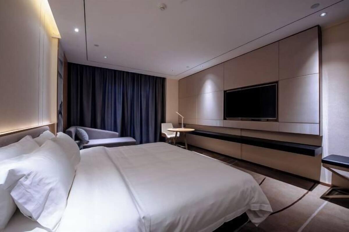 Ein modernes Hotelzimmer mit einem großen Bett, einem flachbildfernseher an der Wand, einem Schreibtisch und einem Sessel.