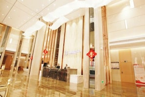 A hotel reception area with a reception desk, a vertical banner with text, and a large mirror reflecting the interior.