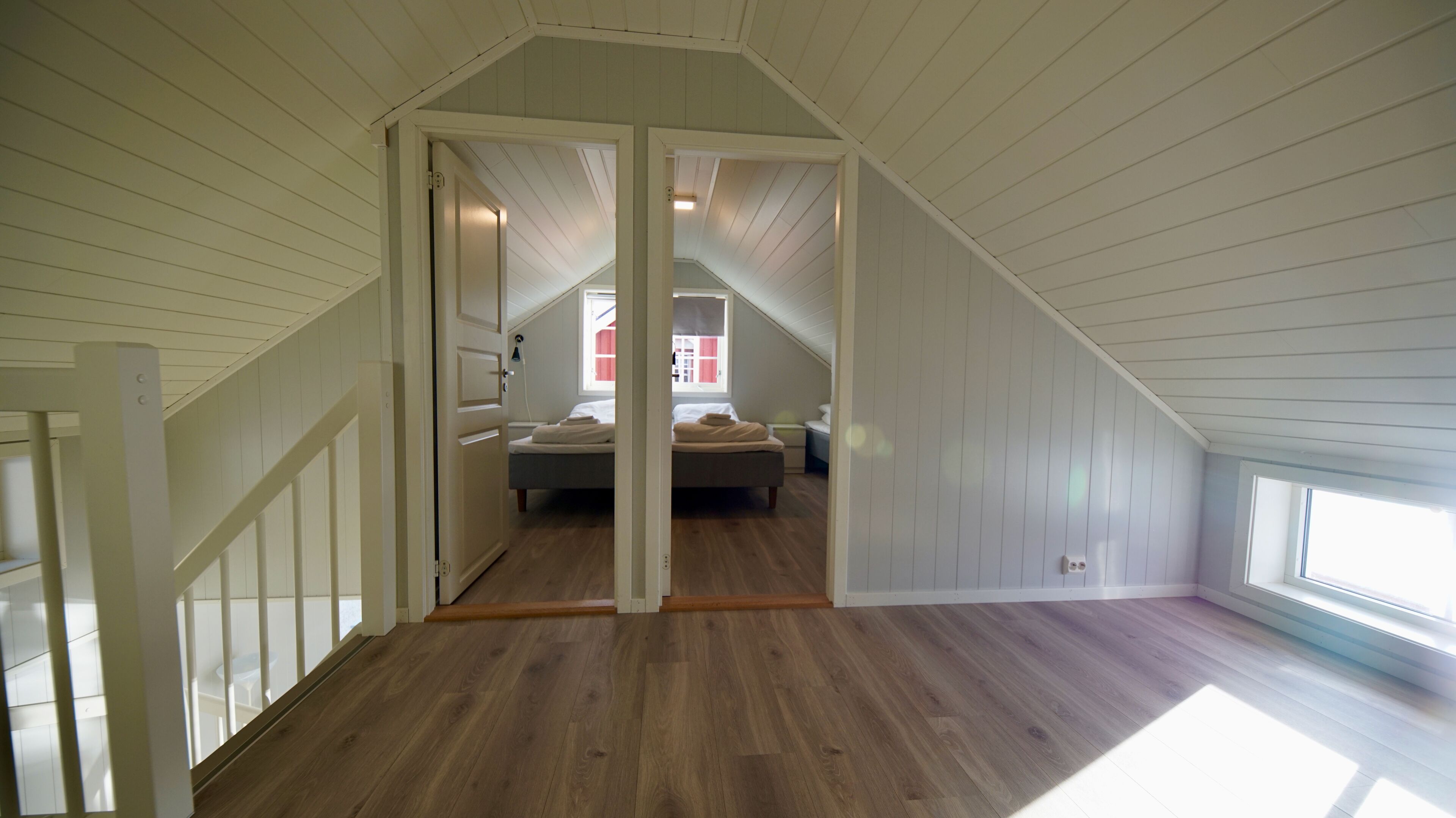 A bedroom with a sloped ceiling, wooden flooring, a bed, and a window.