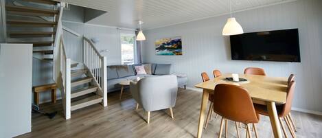 Ein modernes Wohnzimmer mit Essbereich, einer Couch, einem Fernseher und einer Treppe.