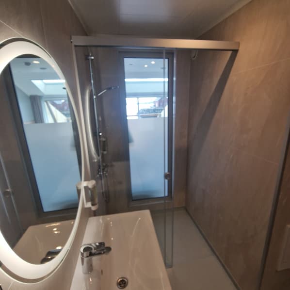A modern bathroom with a large mirror, a sink, and a glass shower enclosure. - Lofoten Basecamp (Vestvågøy)