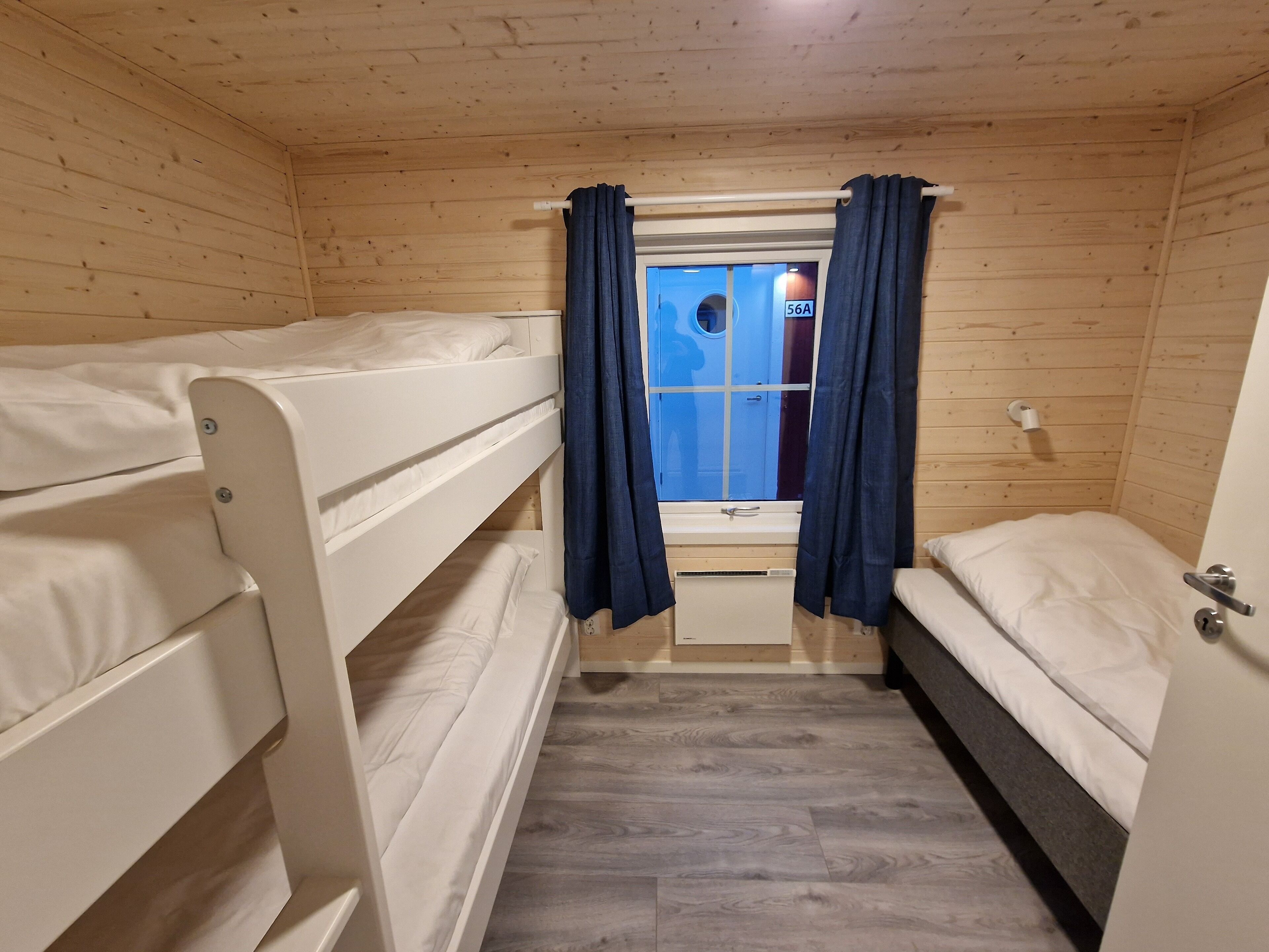 A small, wooden cabin room with bunk beds and a window with curtains.