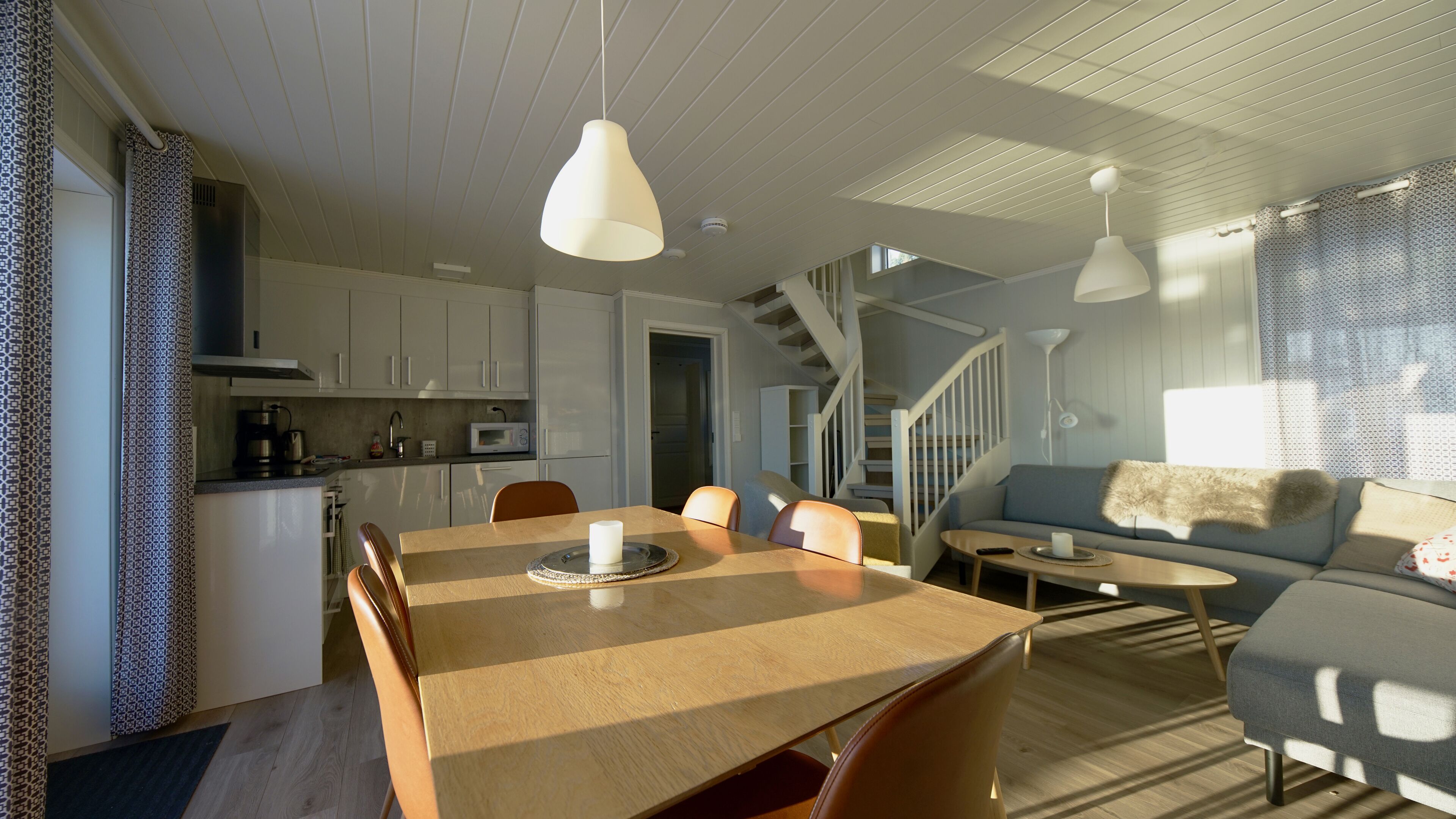 A spacious living area with a wooden dining table, a sofa, and a staircase leading to an upper floor.