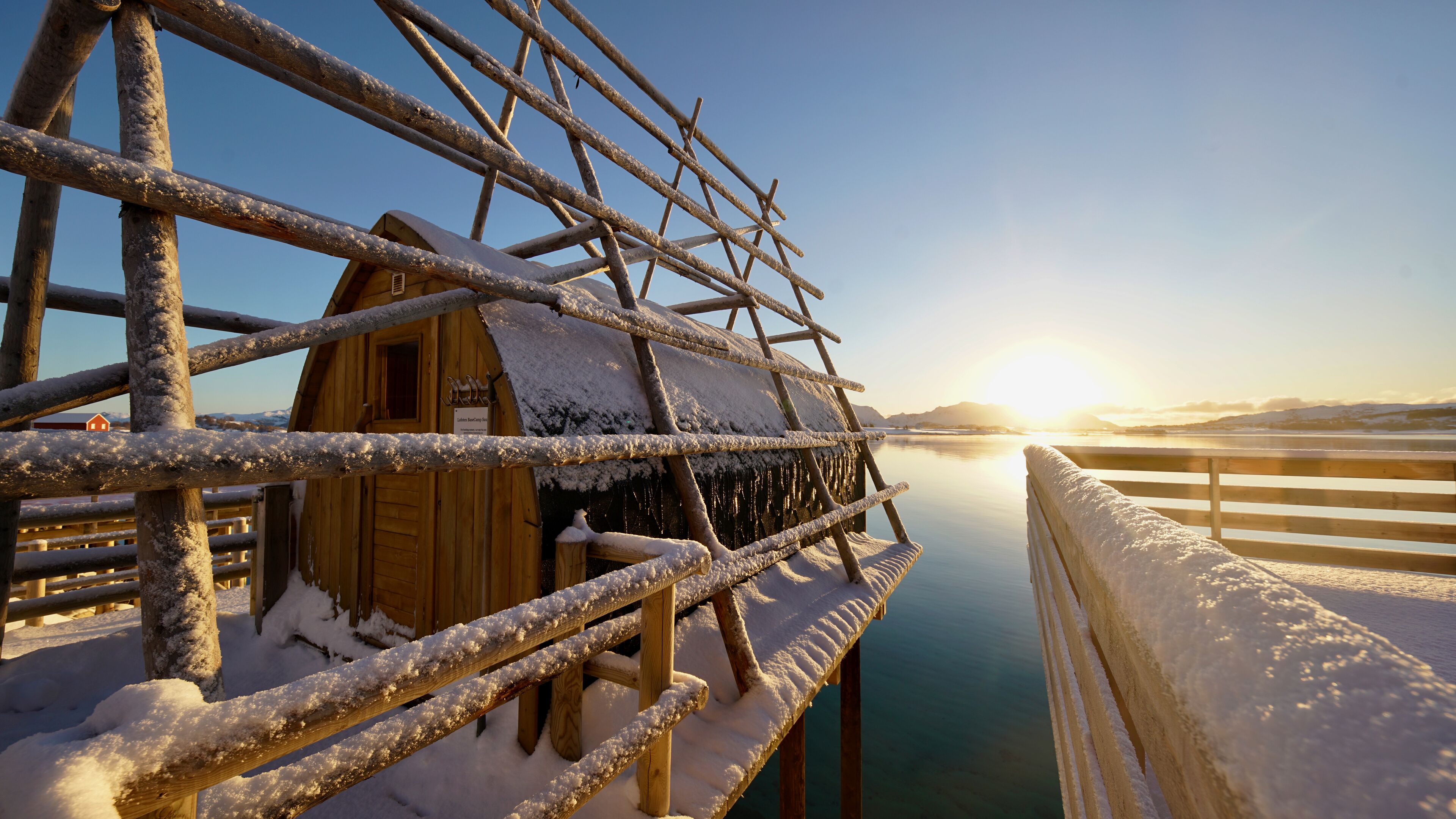 A wooden cabin with a snow-covered roof and a wooden deck extending over a body of water.