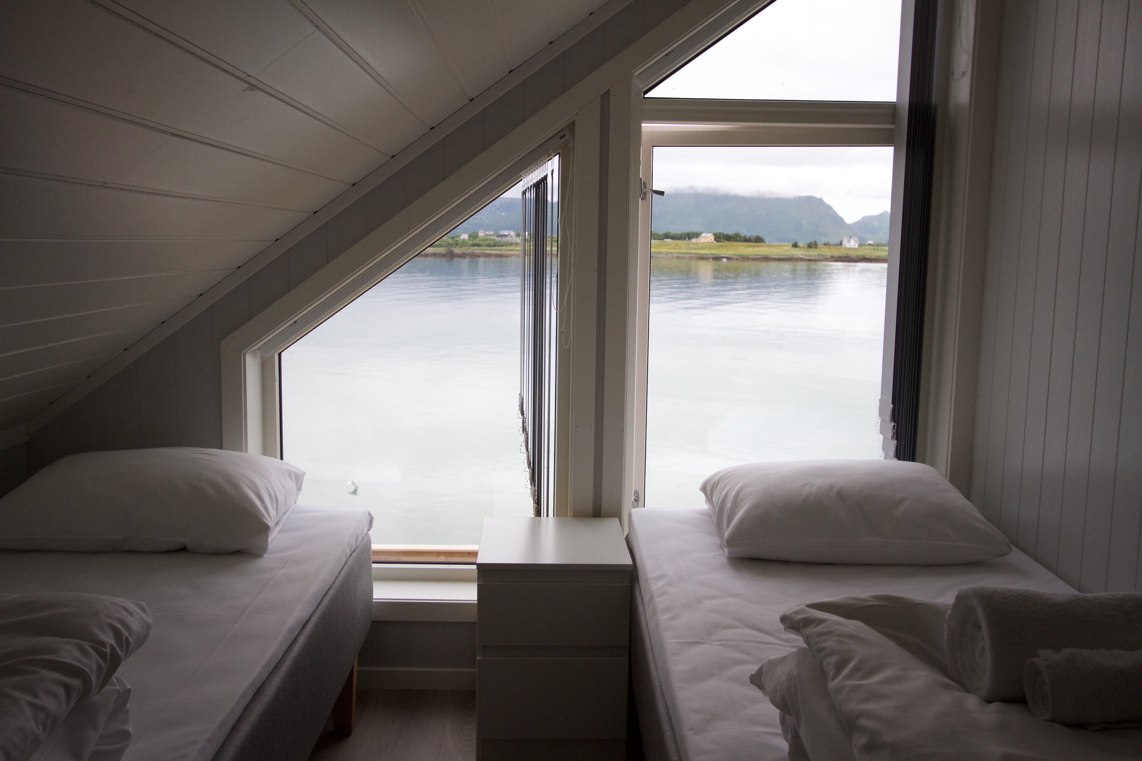 A bedroom with two beds, a window, and a view of a lake and mountains.