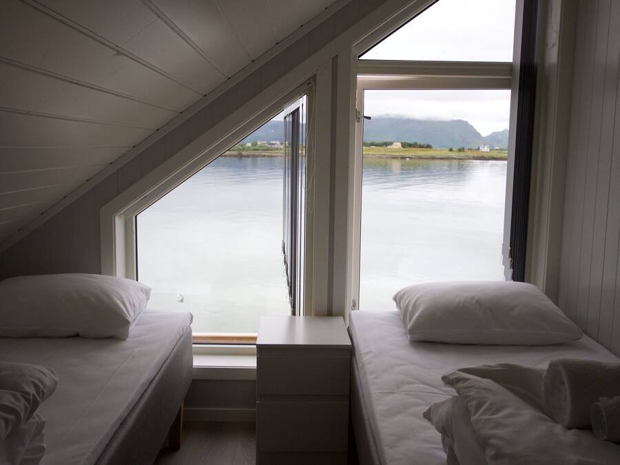 A bedroom with two beds, a window, and a view of a lake and mountains.