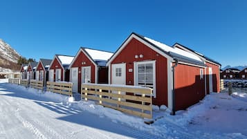 A row of red cabins with white trim, wooden fences, and a clear blue sky.