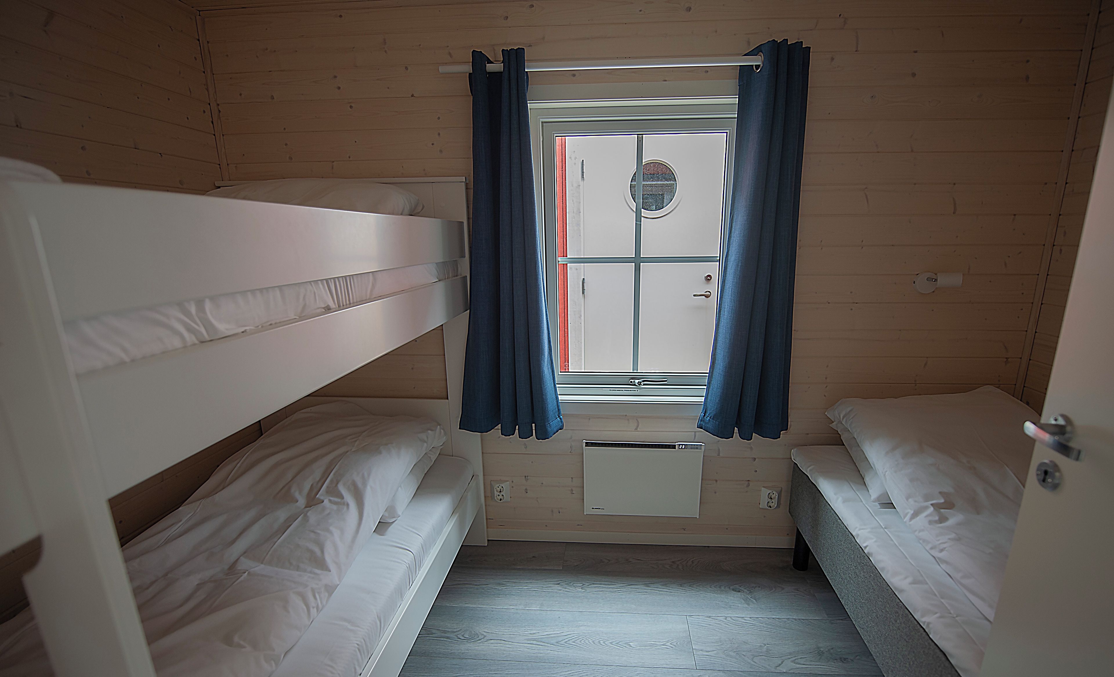 Una cabana amb tres llits individuals, una finestra amb cortines i vista al port.