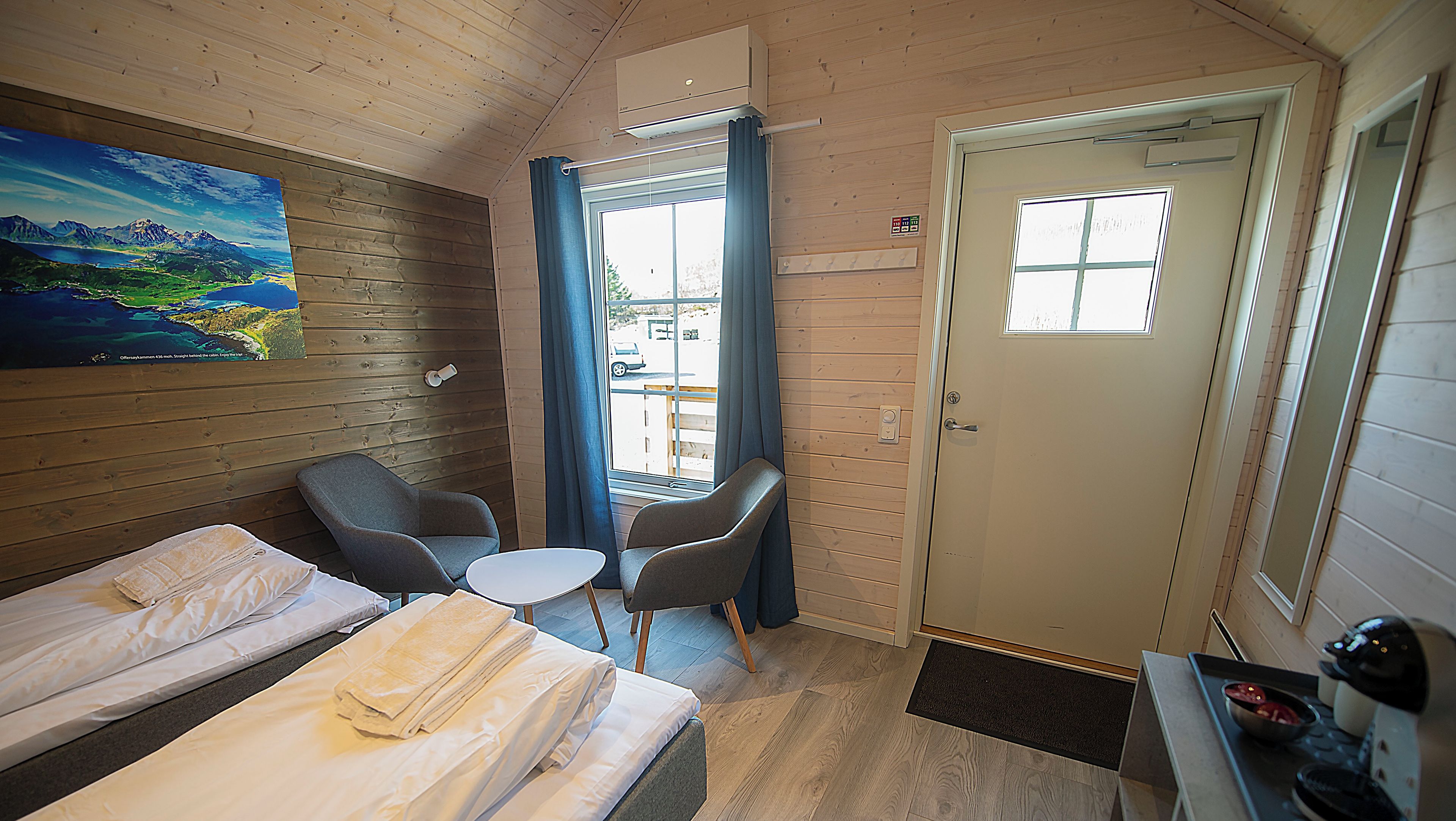 Habitación estándar con dos camas, una mesita, dos sillas, un cuadro en la pared y una ventana con cortinas.