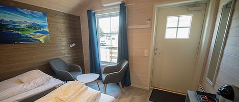 Habitación estándar con dos camas, una mesita, dos sillas, un cuadro en la pared y una ventana con cortinas.