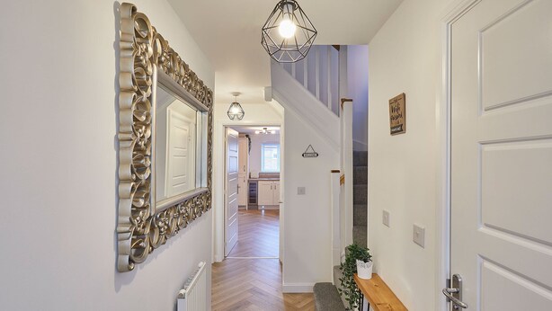 Un pasillo con un espejo decorativo, un banco, un cartel de bienvenida y una escalera que conduce a otra habitación.