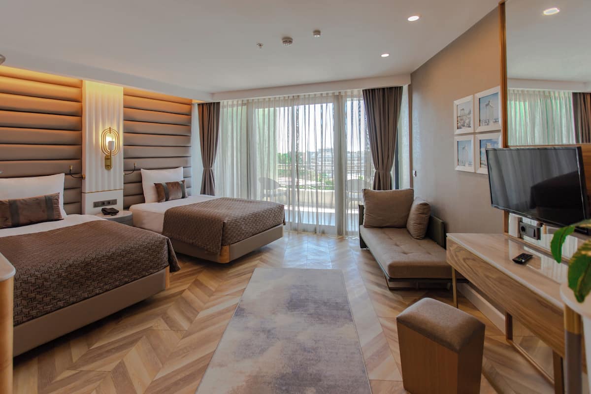 A hotel room with two beds, a sofa, a TV, and a desk.