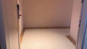 Un pasillo estrecho con alfombra blanca, suelo de madera y una puerta blanca a la izquierda.