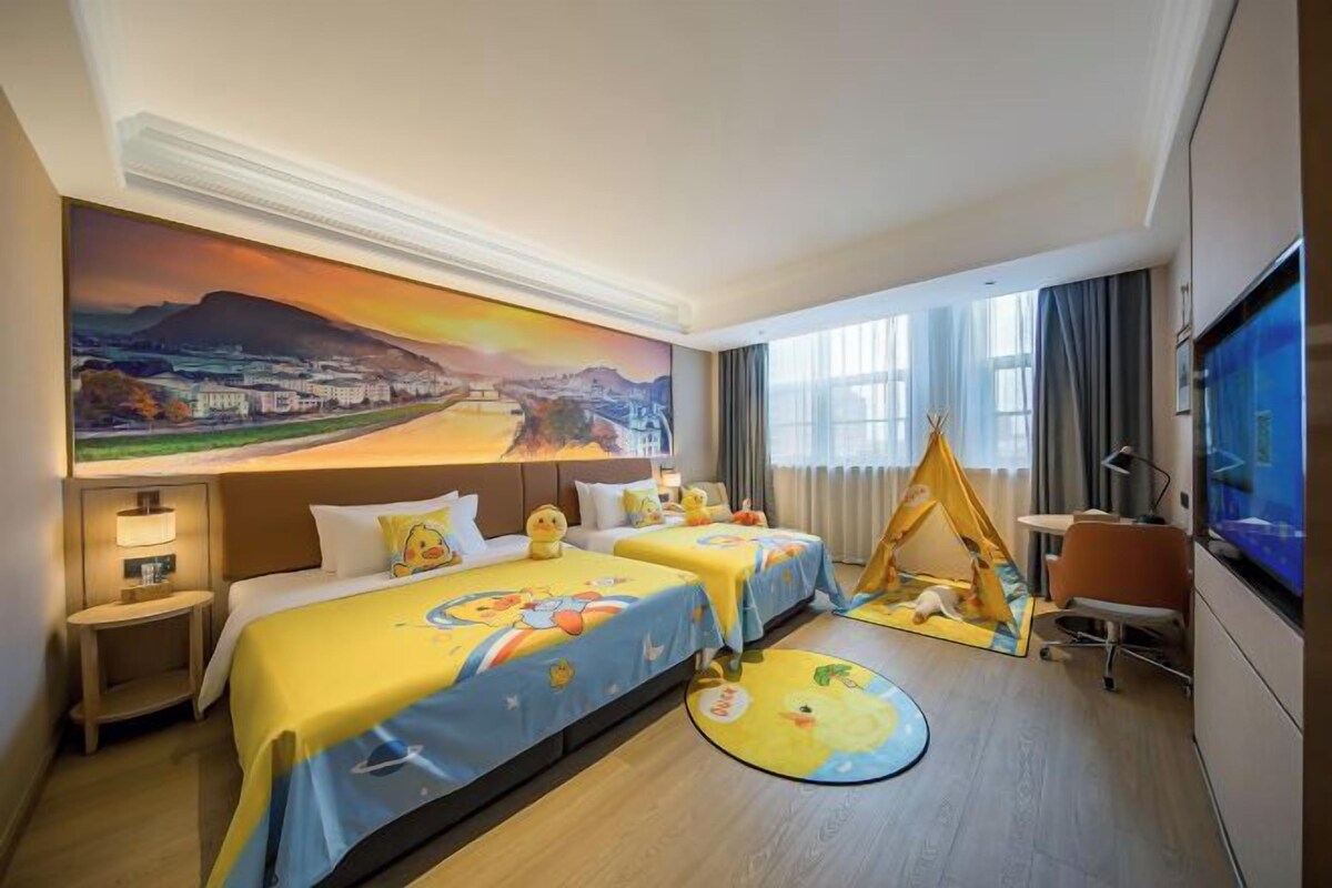 A hotel room with two beds, a large mural, a TV, and a play area.
