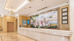 Un vestíbulo con suelo de mármol, un mostrador de recepción, un mural y certificados enmarcados en la pared.