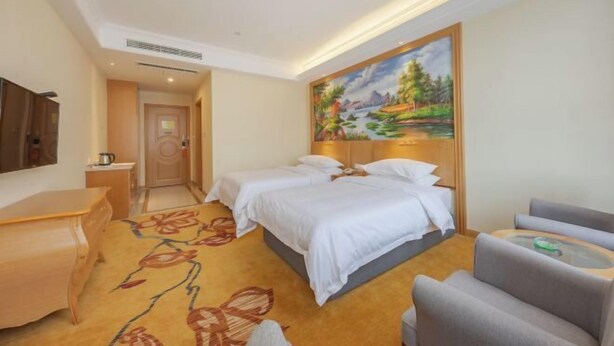 Habitación de hotel con dos camas, un escritorio, una silla y un cuadro en la pared.