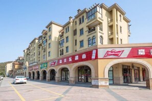 A multi-story building with a row of shops on the ground floor, including a Budweiser sign. - Vienna Hotel (Zhoushan)