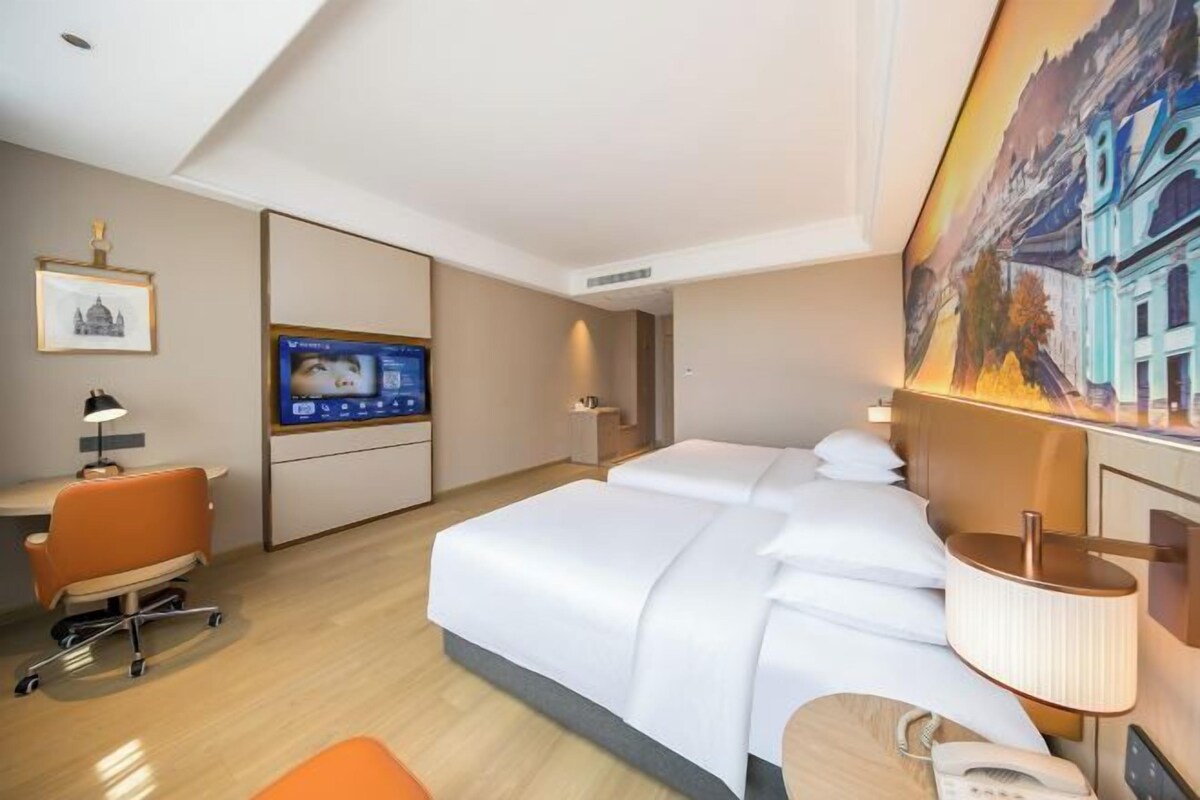 Une chambre d’hôtel avec un lit, un bureau, une chaise, une télévision et un tableau au mur.