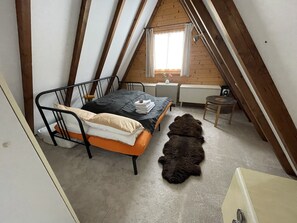Une chambre à coucher avec un lit, une petite table, une chaise, une fenêtre et un tapis en fourrure.