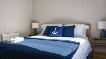 A hotel room with a bed, two bedside tables, a lamp on each table, a blue and white bedspread, and a blue throw blanket.