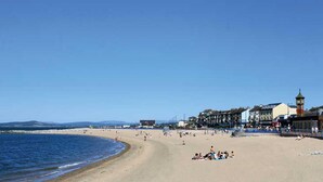 Une plage avec un ciel dégagé, un rivage sablonneux et des bâtiments en arrière-plan.