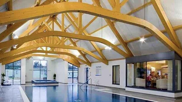 Une piscine intérieure dotée d’un haut plafond en bois et offrant une vue dégagée sur l’extérieur.