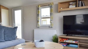 Un salon comprenant un canapé, une table basse ronde en bois, un téléviseur et une étagère remplie de livres et de jeux.