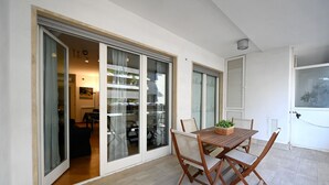Una sala moderna con una mesa y sillas de madera, una puerta corrediza de vidrio que da a otra habitación, y una pared blanca con una ventana.