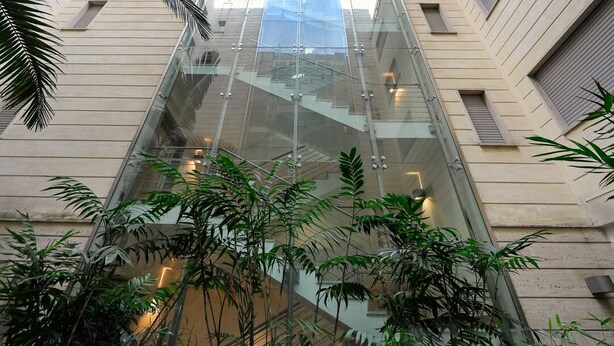 Un edificio moderno con un ascensor de vidrio y vegetación circundante.