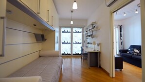Habitación de hotel compacta con cama, escritorio y silla. Hay una ventana con vistas a edificios y un sofá en la esquina.