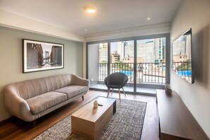 A modern living room with a sofa, a coffee table, and a chair. There is a large window with a view of buildings and a balcony. - w* | Perfect 2BR with Balcony in Miraflores (Lima)