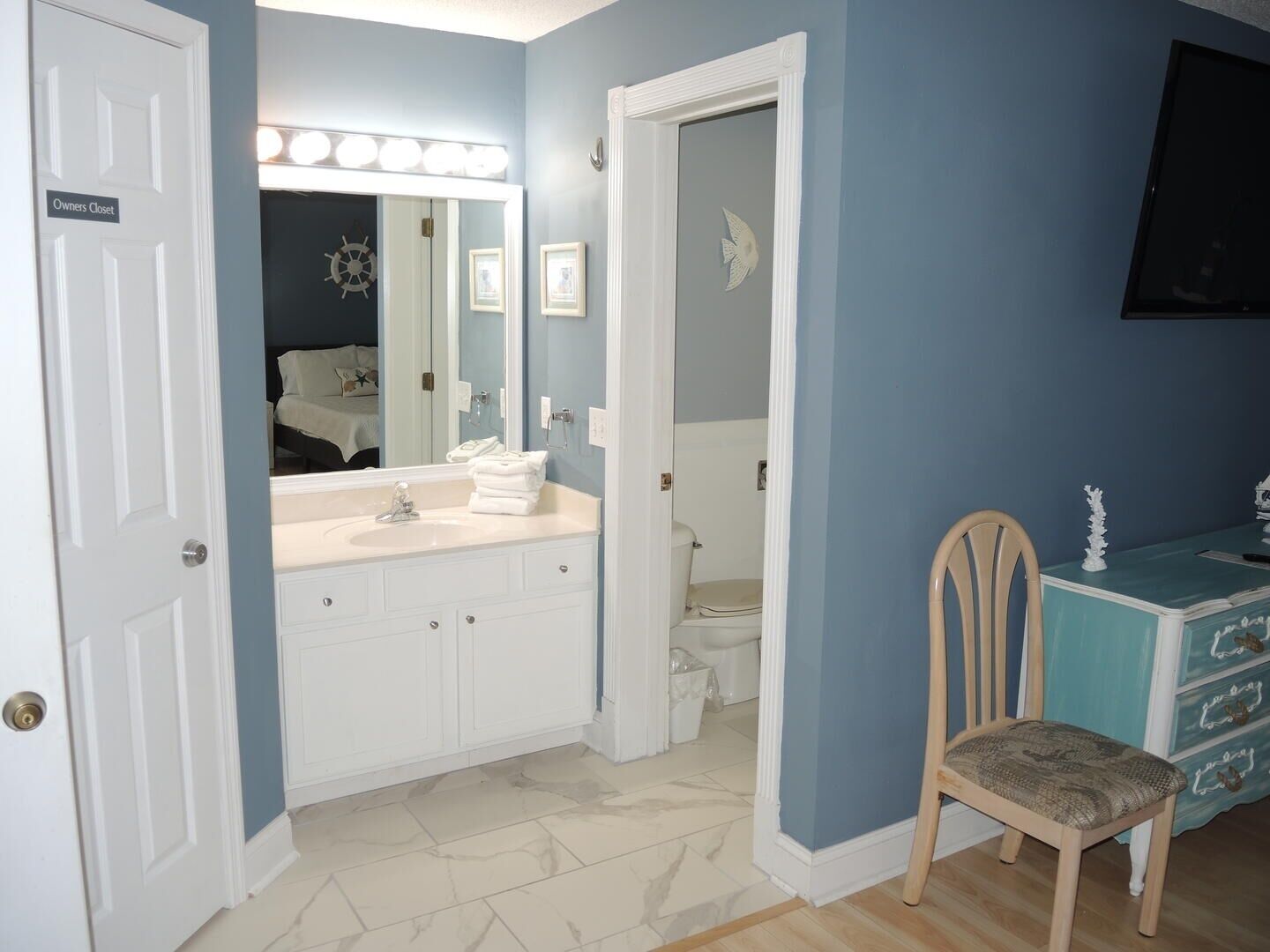 A bathroom with a vanity, sink, and mirror. There is a chair and a dresser with drawers.