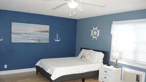 A bedroom with a bed, a nightstand, a ceiling fan, a window with blinds, and nautical-themed wall decor.