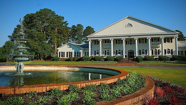 A large, symmetrical building with a central entrance flanked by columns, a fountain in the foreground, and a well-maintained lawn.
