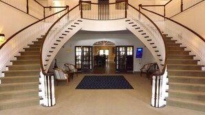 A grand staircase with a central landing, flanked by two sets of chairs, leading to a reception area with a digital display.