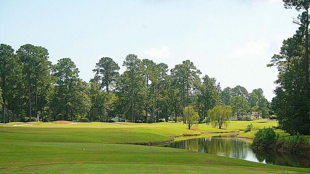 A golf course with a pond, trees, and houses in the background. - Brunswick Plantation Resort and Golf Villa 2705L in the Heart of NC Seafood Country by RedAwning (Calabash)