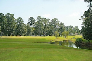 A golf course with a pond, trees, and houses in the background. - Brunswick Plantation Resort and Golf Villa 2705L in the Heart of NC Seafood Country by RedAwning (Calabash)
