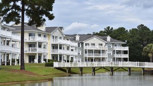 A multi-story hotel with balconies, a dock over water, and a grassy area. - Brunswick Plantation Resort and Golf Villa 2705L in the Heart of NC Seafood Country by RedAwning (Calabash)