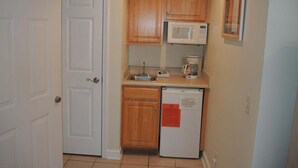 A compact kitchen with wooden cabinets, a microwave, a coffee maker, and a refrigerator. - Brunswick Plantation Resort and Golf Villa 2705L in the Heart of NC Seafood Country by RedAwning (Calabash)
