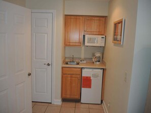 A compact kitchen with wooden cabinets, a microwave, a coffee maker, and a refrigerator. - Brunswick Plantation Resort and Golf Villa 2705L in the Heart of NC Seafood Country by RedAwning (Calabash)