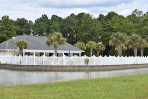 A house with a white picket fence, a covered porch, and a body of water in front. - Brunswick Plantation Resort and Golf Villa 2705L in the Heart of NC Seafood Country by RedAwning (Calabash)