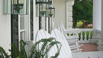 A porch with white chairs and a potted fern.