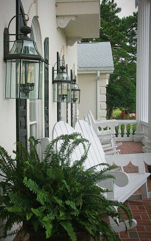 A porch with white chairs and a potted fern. - Brunswick Plantation Resort and Golf Villa 2705L in the Heart of NC Seafood Country by RedAwning (Calabash)