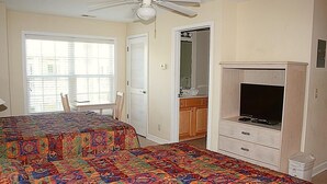A bedroom with a bed, a television, a ceiling fan, and a window with blinds.