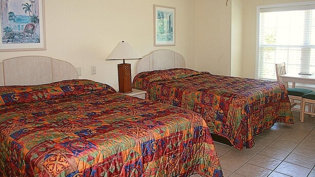 A room with two beds, a ceiling fan, a table with chairs, and a window with blinds.