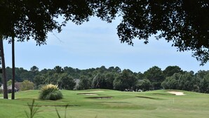 Un campo de golf con búnkeres de arena, una bandera y un club de campo al fondo.