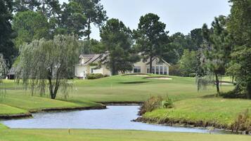 A golf course with a pond, trees, and a house in the background.